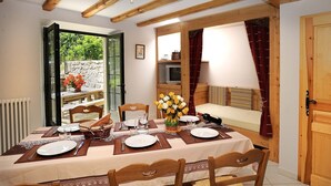Un comedor con una mesa dispuesta para cuatro, sillas de madera, un florero y un televisor al fondo.