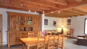 A wooden dining table with chairs, a kitchen with wooden cabinets, a sofa, and a lamp.
