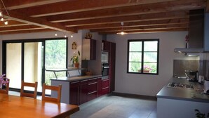A modern kitchen with wooden beams, a dining area with a table and chairs, and a window with a view of greenery.