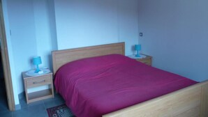A bedroom with a wooden bed, a nightstand with a lamp, and a small drawer unit.