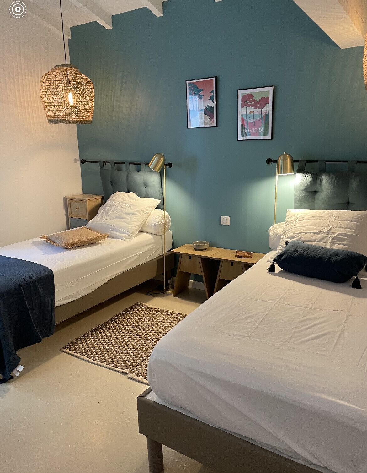 Une chambre avec deux lits, un luminaire en matière tressée et deux tableaux encadrés accrochés au mur.