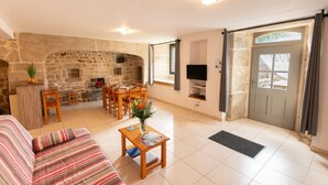 A cozy living room with a stone fireplace, a dining area, and a TV mounted on the wall. - 4/6 person gîte at Ferme Lionnet (ALBARET LE COMTAL)