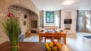A stone archway leading to a dining area with a table set for four, a fruit bowl on the table, and a television in the room. - 4/6 person gîte at Ferme Lionnet (ALBARET LE COMTAL)