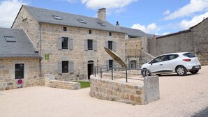 A stone building with multiple windows and a car parked in front. - 4/6 person gîte at Ferme Lionnet (ALBARET LE COMTAL)