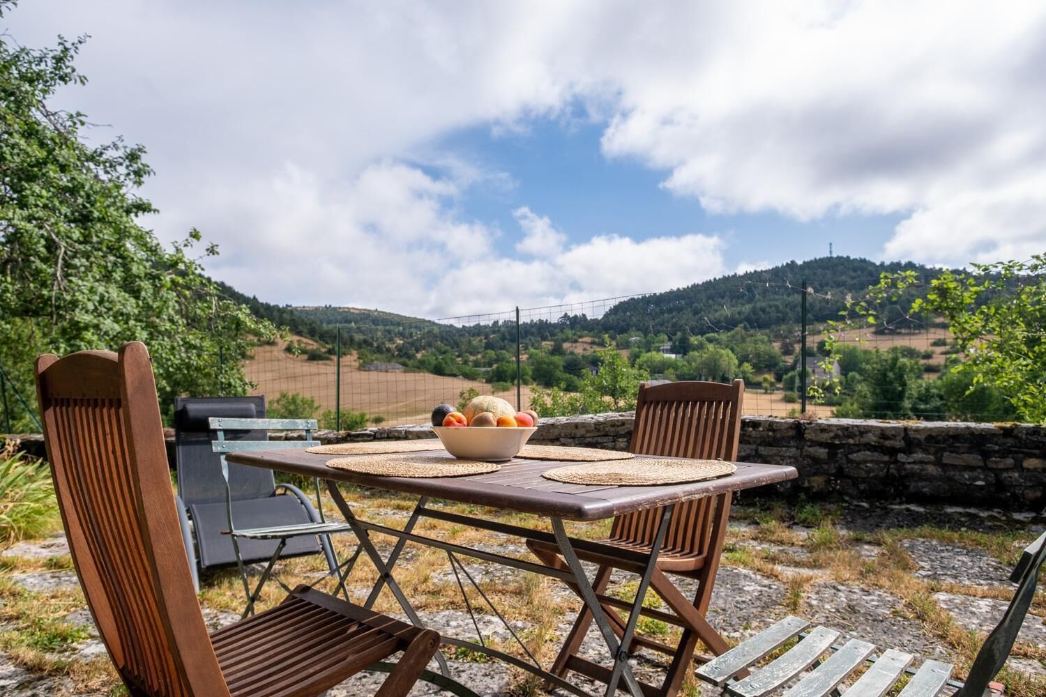 Un espace extérieur aménagé pour prendre les repas, avec une table, des chaises et un saladier rempli de fruits.