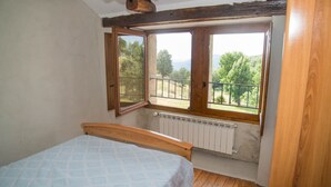 A bedroom with a wooden bed, a window with a view of greenery, and a radiator. - Gîtes de France 3/5 people in La Bessière (PIED DE BORNE)