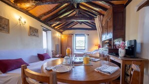 Une pièce chaleureuse avec un plafond en bois, une table ronde en bois, un lit avec un oreiller violet et un téléviseur posé sur un meuble en bois.