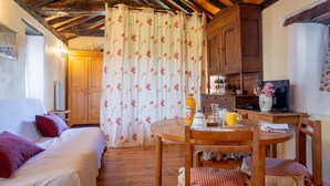 Une pièce chaleureuse avec un plafond en bois, un lit agrémenté d’oreillers rouges, une table à manger avec des chaises, et un coin cuisine doté de placards en bois.