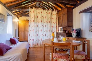 Ein gemütliches Zimmer mit Holzbalkendecke, einem Bett mit roten Kissen, einem Esstisch mit Stühlen und einer Küchenzeile mit Holzschränken.