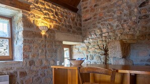 A rustic stone interior with a wooden table and chairs, a wall-mounted light fixture, and a coat rack. - Le Four, Ferme de la Beyssiere (PIED DE BORNE)