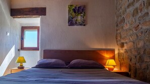 A bedroom with a wooden headboard, a bed with a striped bedspread, two nightstands with lamps, a window, and a wall-mounted painting of flowers. - Le Four, Ferme de la Beyssiere (PIED DE BORNE)