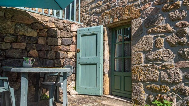 A stone building with a green door and a small table with chairs outside. - Le Four, Ferme de la Beyssiere (PIED DE BORNE)