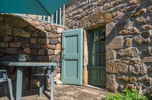 Un edificio de piedra con una puerta verde y una pequeña mesa con sillas afuera.