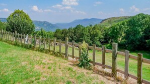 A rural landscape with a wooden fence, green fields, and distant mountains under a clear sky. - Le Four, Ferme de la Beyssiere (PIED DE BORNE)