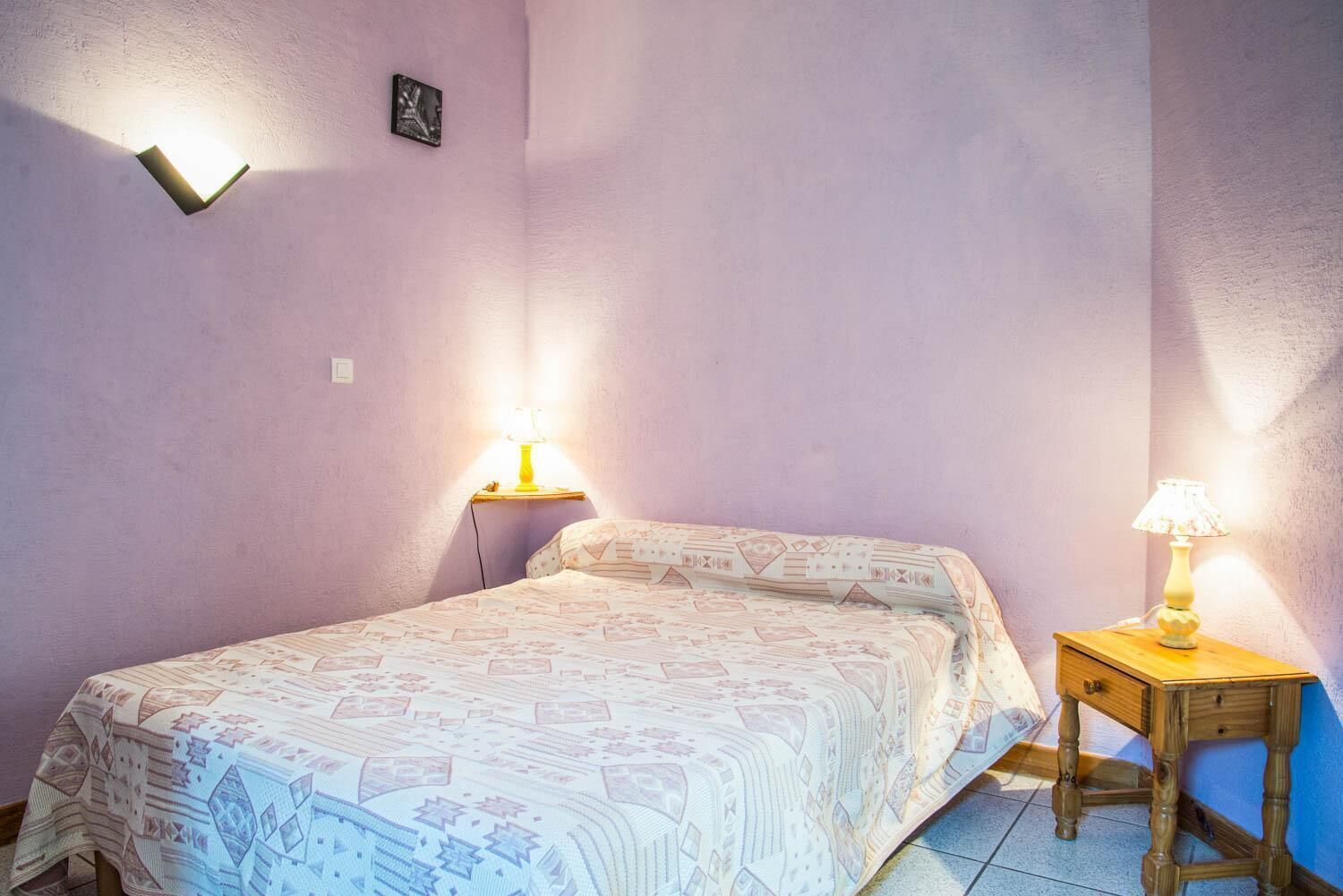 A bedroom with a bed, two bedside tables with lamps, and a wall-mounted light fixture.