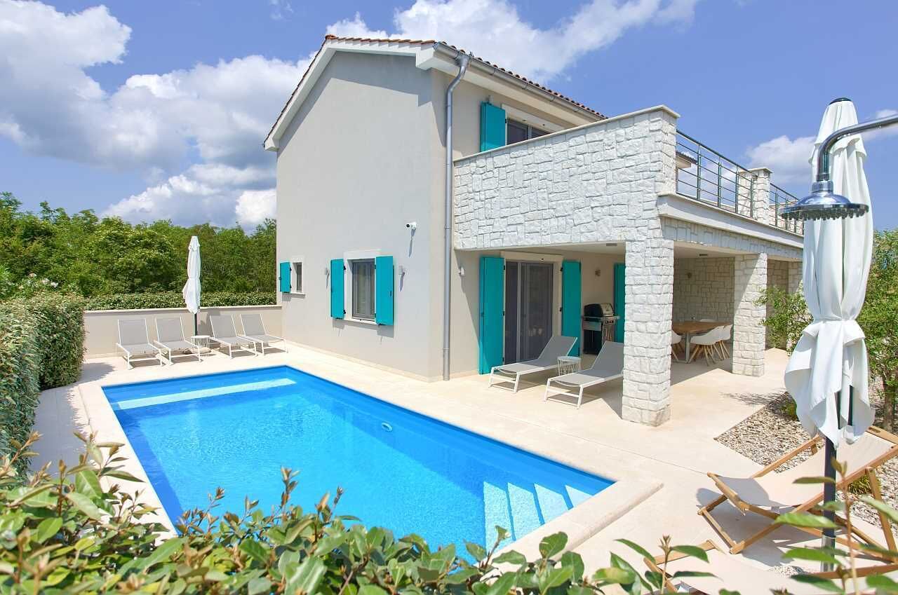 A two-story house with a swimming pool, outdoor seating, and a stone facade.