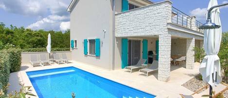 A two-story house with a swimming pool, outdoor seating, and a stone facade.