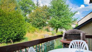 A patio with a chessboard, a grill, and a view of trees and a stone wall.