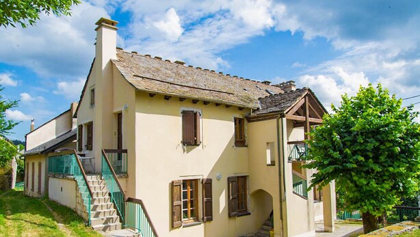 A traditional two-story house with a steeply pitched roof, a visible chimney, and a small staircase leading to the entrance.