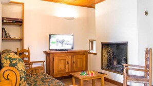 A cozy living room with a television, wooden furniture, a fireplace, and a bookshelf.