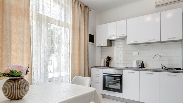 A modern kitchen with white cabinets, a built-in oven, and a window with sheer curtains. - Apartments K & N -One Bedroom Apartment A2 (Prižba)