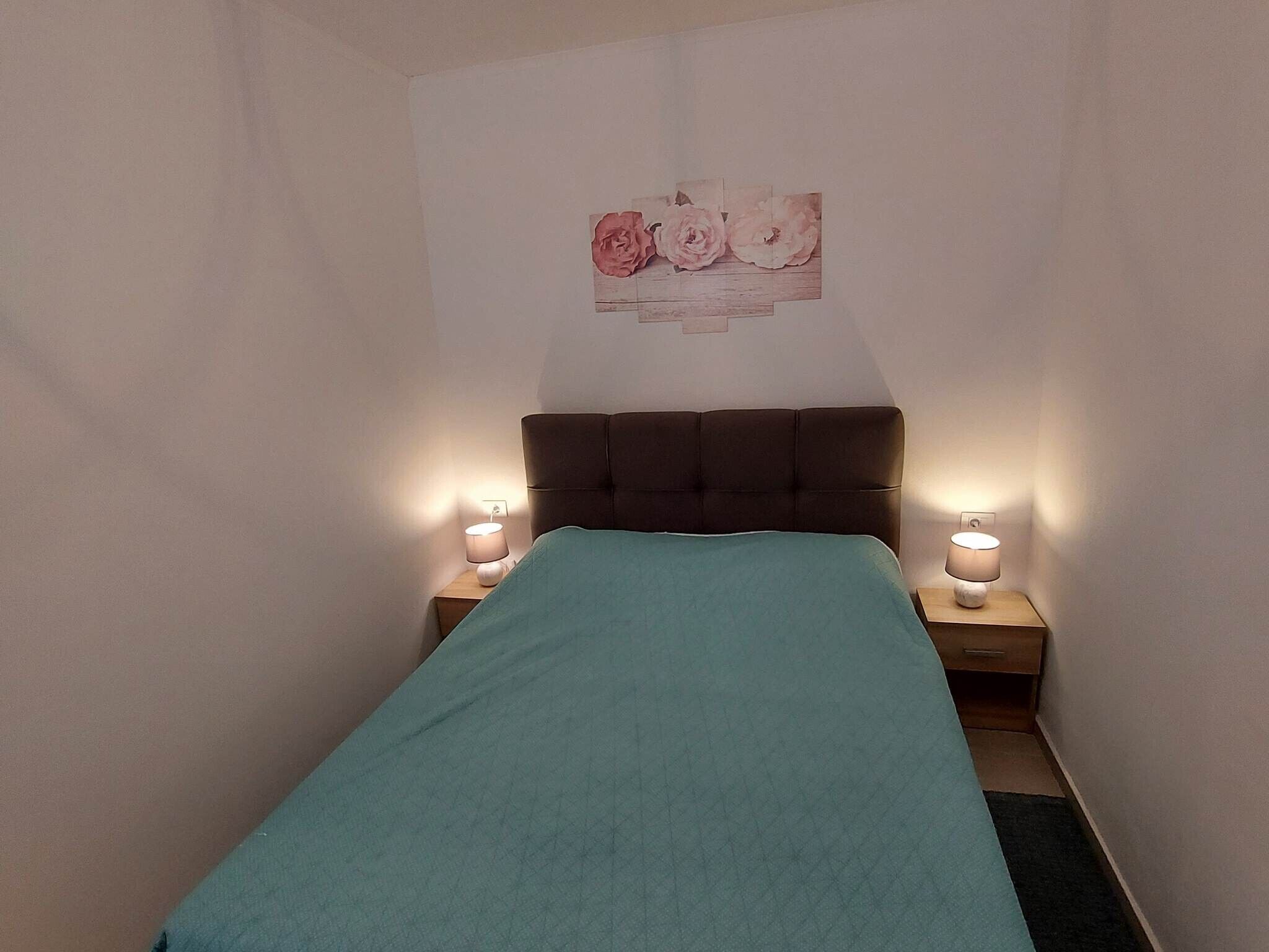 A small, neatly arranged bedroom with a single bed, two bedside tables, and a wall-mounted artwork.