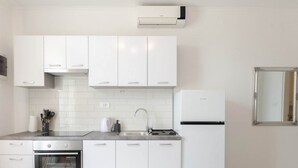 A modern kitchen with white cabinetry, a built-in oven, a refrigerator, and a wall-mounted air conditioner. - Apartments K & N -One Bedroom Apartment A2 (Prižba)