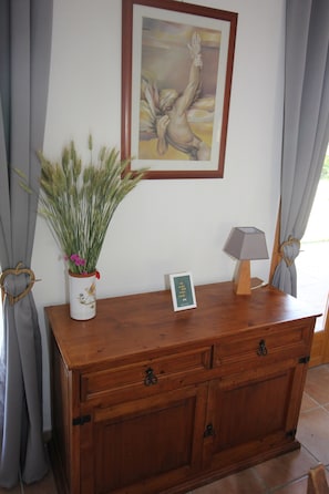 A wooden cabinet with a vase of green plants and a framed picture on the wall.