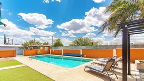 Una piscina con sillones de descanso, un área de césped y un muro de ladrillo.