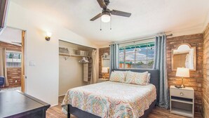 Un dormitorio con cama, mesitas de noche, ventilador de techo y vistas al exterior.
