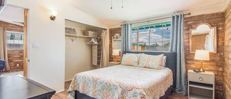 Een slaapkamer met een bed, nachtkastjes, een plafondventilator en uitzicht door een raam.