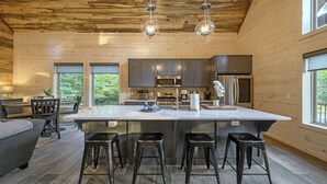 A modern kitchen with a large island, stainless steel appliances, and a wooden interior. - Sweet Caroline Creek-Side Cabin 🎯  Games 🔥 Hot Tub 📺 Outdoor TV (BROKEN BOW)