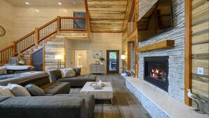 A spacious living room with a fireplace, wooden staircase, and comfortable seating. - Sweet Caroline Creek-Side Cabin 🎯  Games 🔥 Hot Tub 📺 Outdoor TV (BROKEN BOW)