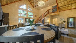 A spacious wooden interior with a dining area, kitchen, and a staircase leading to an upper level. - Sweet Caroline Creek-Side Cabin 🎯  Games 🔥 Hot Tub 📺 Outdoor TV (BROKEN BOW)
