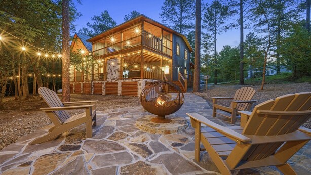 A cabin with a stone patio, wooden deck, and outdoor seating. - Sweet Caroline Creek-Side Cabin 🎯  Games 🔥 Hot Tub 📺 Outdoor TV (BROKEN BOW)