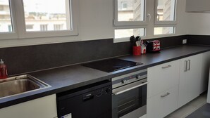 A modern kitchen with a dishwasher, oven, and a window with a view of buildings. - Grand Logement Rénové, 84 m2, 5 Personnes, à 100 m de la Gare et du Tramway (Le Havre)