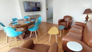 A dining area with a round table, blue and brown chairs, and a television mounted on the wall. - Grand Logement Rénové, 84 m2, 5 Personnes, à 100 m de la Gare et du Tramway (Le Havre)