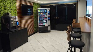 Um interior moderno com uma máquina de vendas, um balcão com bancos e uma parede verde.