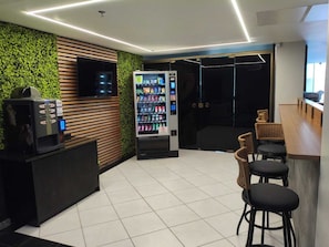 A modern interior with a vending machine, a counter with stools, and a green wall. - Loft in Prainha - Ocean View and Sunrise (Arraial do Cabo -Prainha)