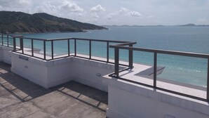 Varanda de concreto com guarda-corpo de metal, vista para um corpo d'água e paisagem montanhosa.