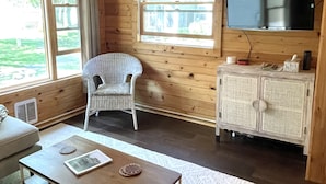 Ein Holzblockhaus-Innenraum mit einer Couch, einem Esstisch, einem Korbstuhl, einem Fernseher und einem Schrank.