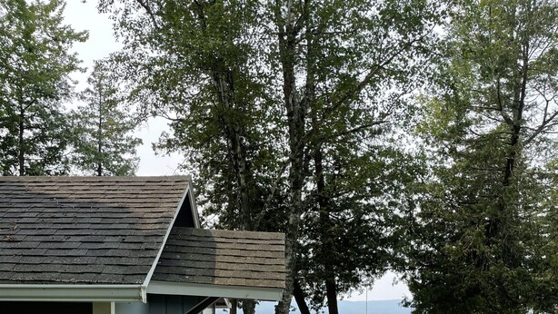 Eine Holzterrasse mit Sitzgelegenheiten im Freien, einem überdachten Grillbereich und Blick auf den See.