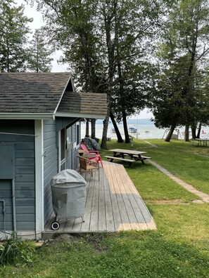 A wooden deck with outdoor seating, a covered grill area, and a view of the lake. - Platte Lake Waterfront Cottage with beach and swimming dock (Honor)