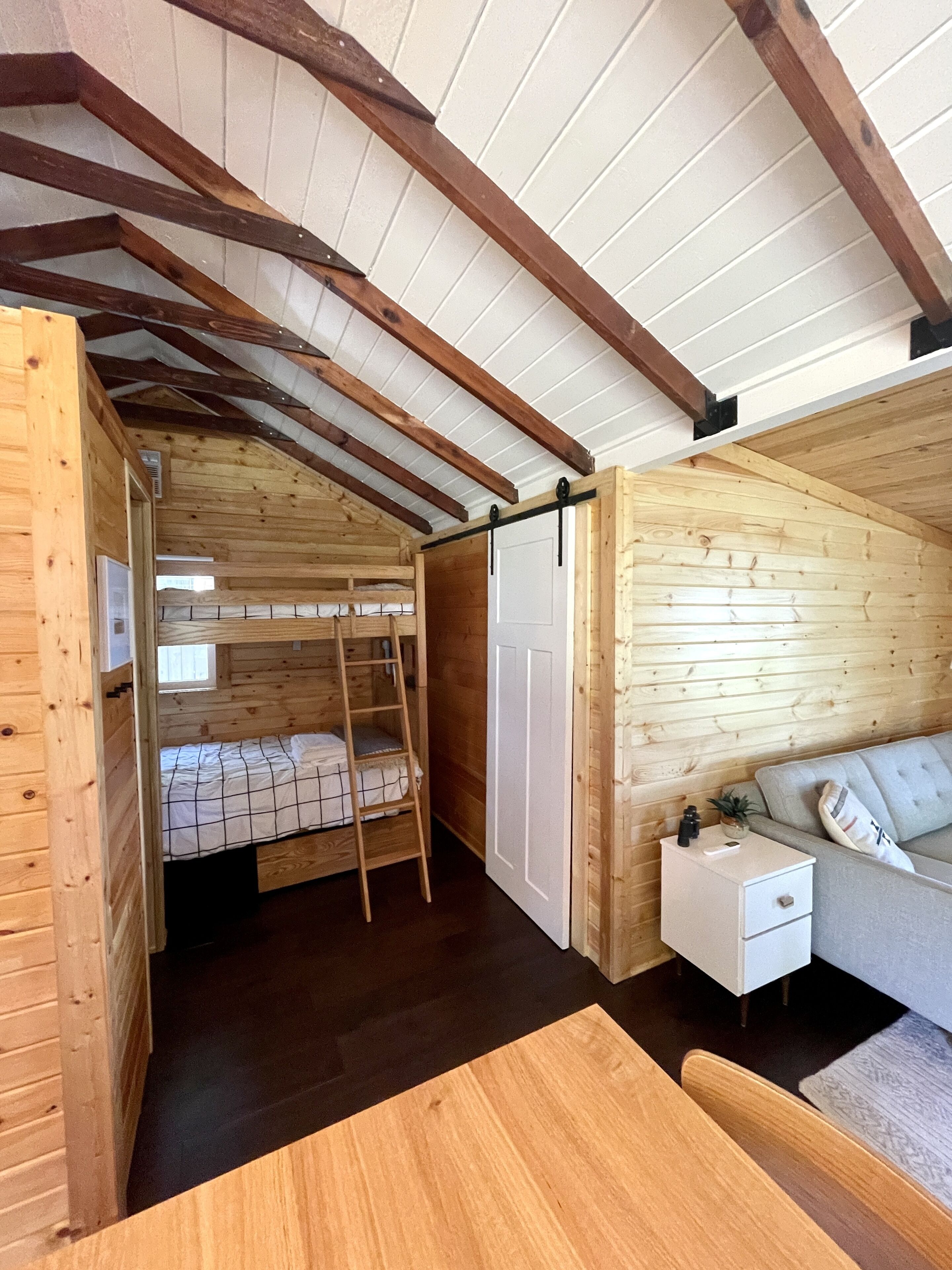 A cozy cabin interior with a wooden interior, a bunk bed, a small white nightstand, and a sofa.