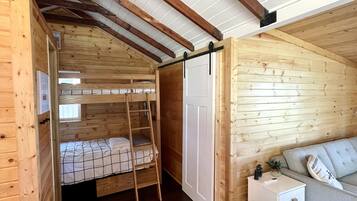 A cozy cabin interior with a wooden interior, a bunk bed, a small white nightstand, and a sofa.