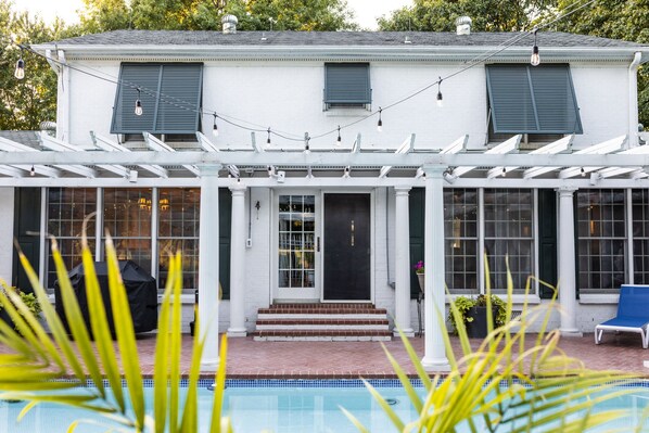 A white building with a covered patio, a pool, and a blue sky.