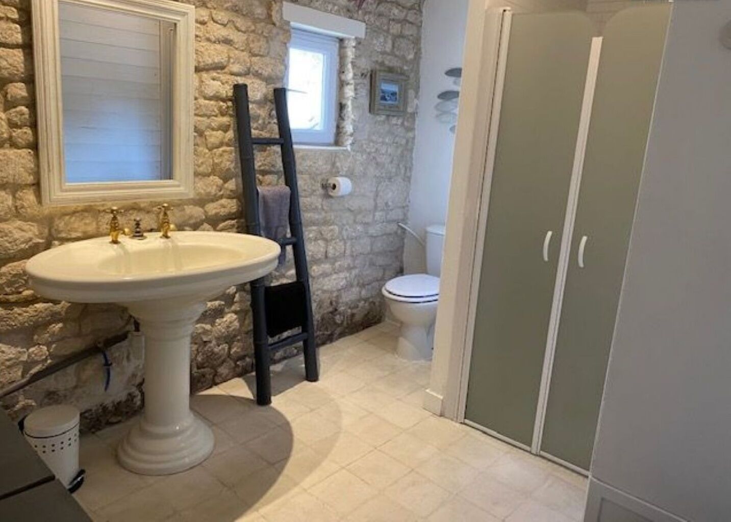 Un baño con pared de piedra, lavamanos pedestal, inodoro y armario.