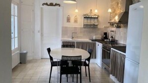 Uma cozinha com mesa de jantar redonda e cadeiras, geladeira branca e piso ladrilhado.