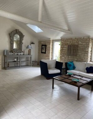 A spacious living room with a high ceiling, stone wall, and a large window.