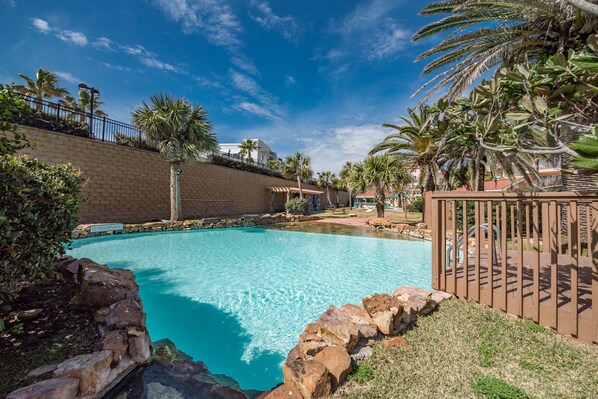 A clear blue pool surrounded by a brick wall, palm trees, and a wooden fence.